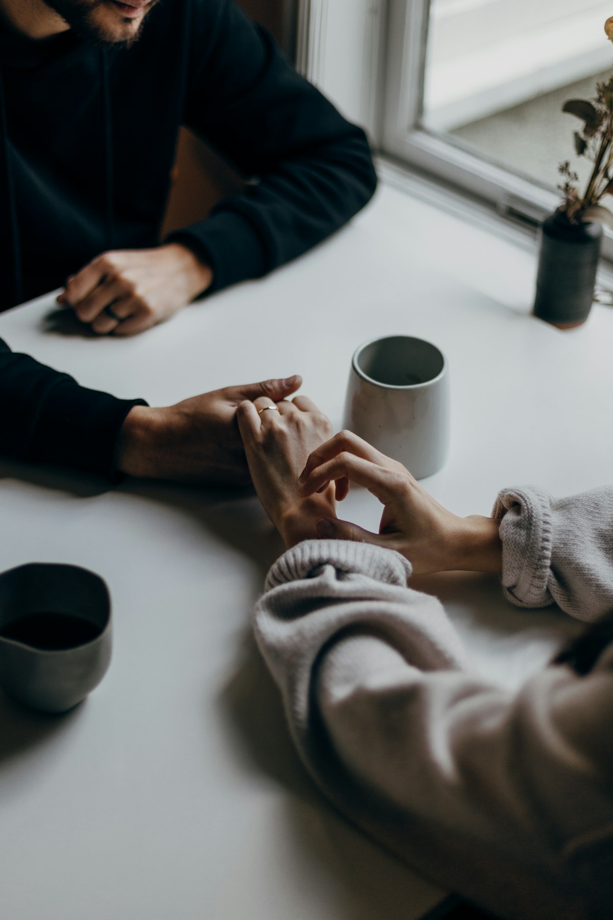 Two people holding hands across a table over coffee